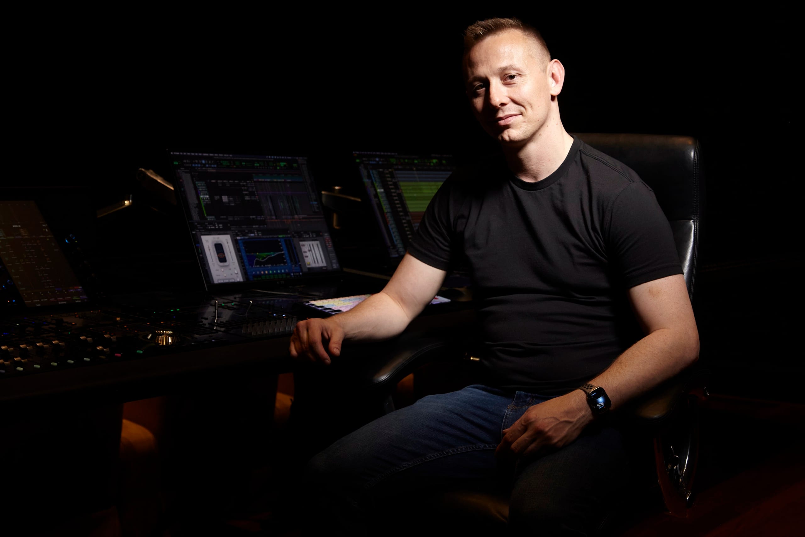 Jason Abell seated at a mixing console on a darkened dub stage, with Pro Tools sessions open on the monitors beside him.
