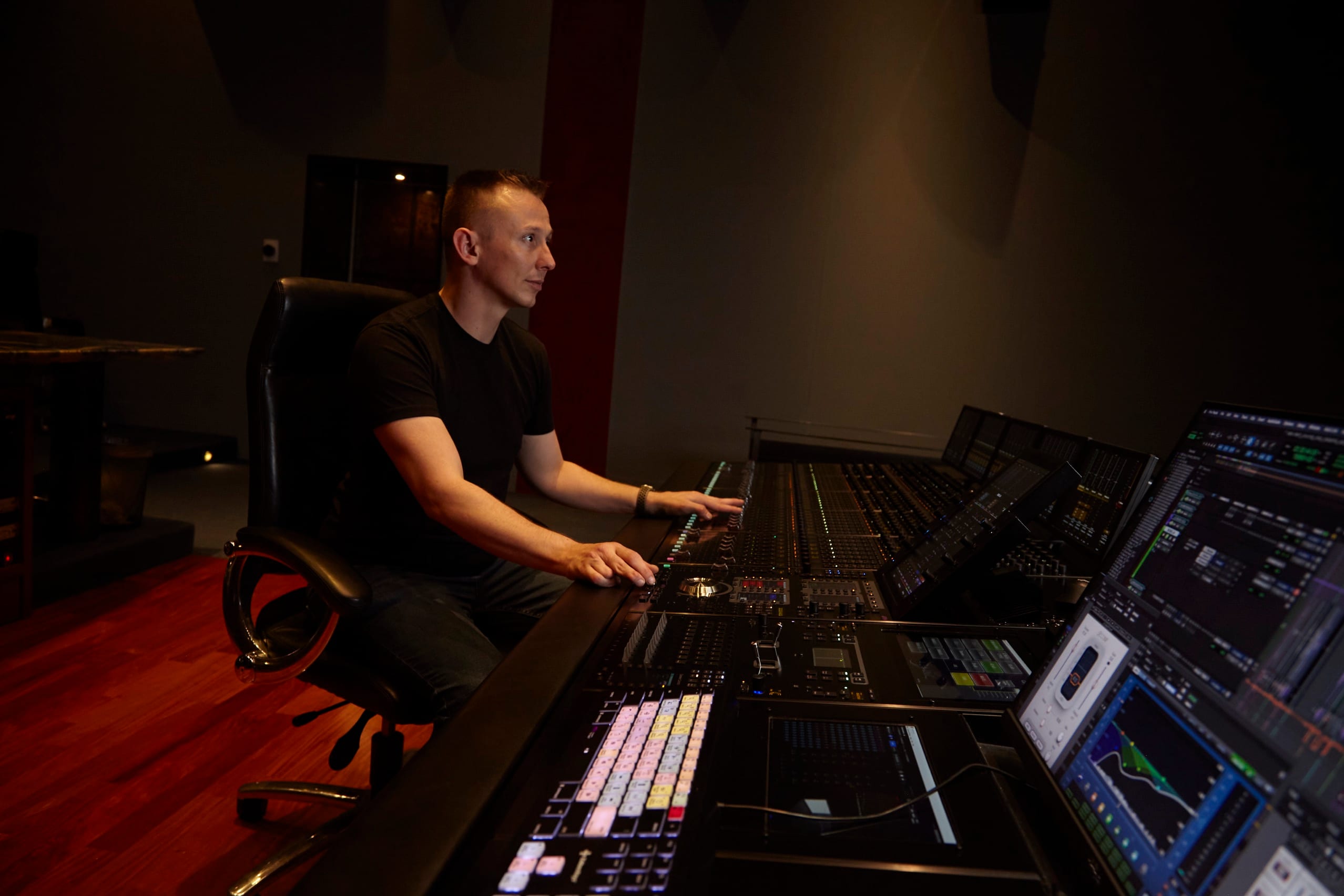 Jason Abell at a mixing console, hands on the control surface, watching the picture on the monitors in front of him.